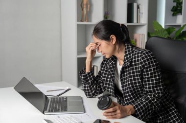 Genç bir muhasebeci, modern ofis ortamında dizüstü bilgisayarla ve kahveyle çalışırken stres yaşıyor..