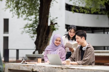 Çeşitli öğrencilerden oluşan bir grup, yaklaşan sınava hazırlanmak üzere dışarıda dizüstü bilgisayarlar ve kitaplarla işbirliği yapıyor ve ders çalışıyor..