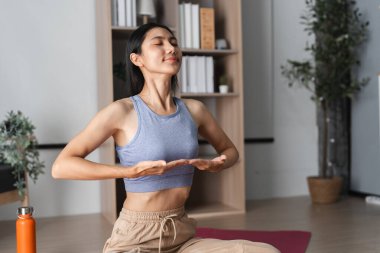 Yoga ve meditasyon yapan genç bir kadın, modern bir ev ortamında rahatlamaya ve farkındalığa odaklanıyor..