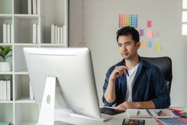 Grafik tasarımcısı, renk örnekleri ve tasarım araçlarıyla çevrili modern bir stüdyoda dijital projelere odaklandı.