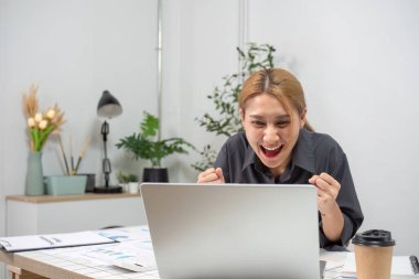 A joyful businesswoman expressing delight at her professional success while working in a contemporary office setting. clipart