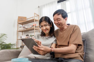 Finans yönetimi için tablet kullanan kıdemli çift, rahat bir ev ortamında takım çalışması ve modern teknoloji sergiliyor..