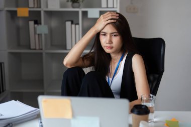 Modern ofis ortamında bir ofis çalışanı dizüstü bilgisayar ve belgelerle masa başında çalışırken stresli görünür..