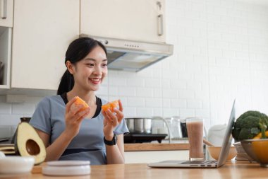 Modern bir mutfakta genç bir kadın sağlıklı bir yaşam tarzı ve sağlığını vurgulayarak besleyici bir meyve kokteyli hazırlıyor..