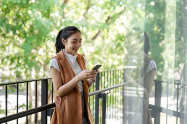 Genç bir kadın, sakin bir şehir ortamında balkonda akıllı telefonuyla iletişim kurmaktan hoşlanıyor..