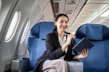 Businesswoman using a tablet on an airplane, showcasing remote work and travel. clipart