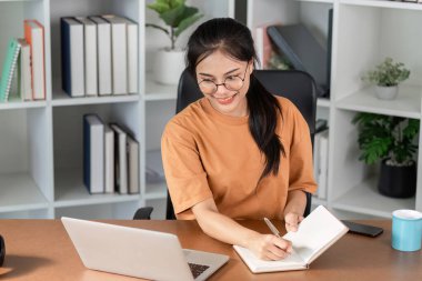 A young woman diligently doing homework at her desk with a laptop and notebook, creating a productive study atmosphere. clipart