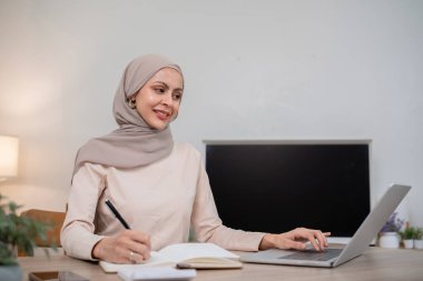 Başörtüsü takan genç bir Müslüman kadın mali hesapları hesaplar. Gelir ve masraflar evdeki oturma odasında..