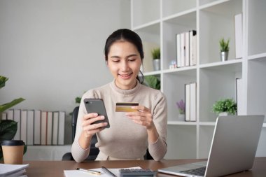 Güzel genç bir kadın internetten alışveriş yapmak için dizüstü bilgisayar kullanıyor, bir şeyler alıyor ve kredi kartıyla internet bankacılığı uygulaması üzerinden ödeme yapıyor...