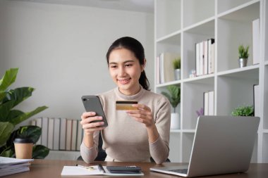 Güzel genç bir kadın internetten alışveriş yapmak için dizüstü bilgisayar kullanıyor, bir şeyler alıyor ve kredi kartıyla internet bankacılığı uygulaması üzerinden ödeme yapıyor...