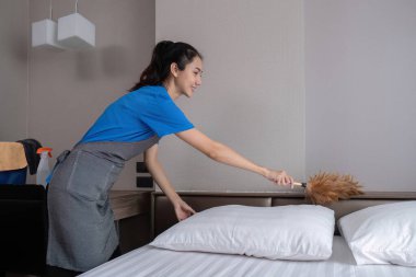 Güzel, genç bir hizmetçi turuncu prezervatifle ev işi yapıyor ve odadaki eşyaları temizlemek için toz bezi kullanıyor...