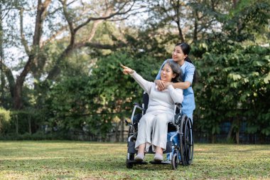 İlgili bir hemşire, sakin bahçe manzarasına hayran olan, tekerlekli sandalyedeki yaşlı bir hastayla oturur..