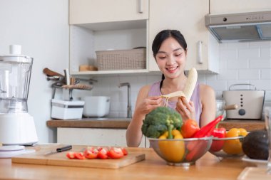 Modern bir mutfakta genç bir kadın taze malzemelerle sağlık ve sağlığa odaklanarak meyve suyu hazırlıyor..
