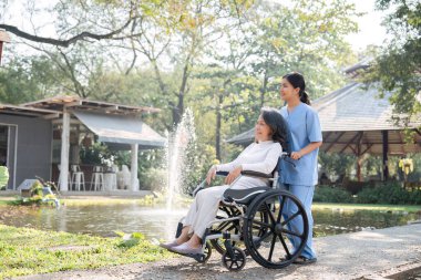 Tekerlekli sandalyedeki bir hemşire ve yaşlı hasta bahçeye hayran, açık havada sakin ve güneşli bir günün tadını çıkarıyor..