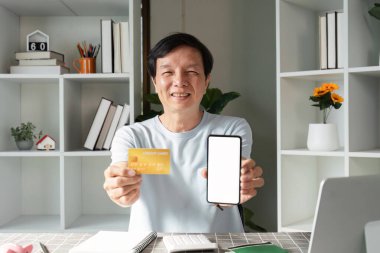 Son sınıf öğrencisi, mutlu bir şekilde kredi kartını akıllı bir telefonun yanında gösteriyor. Ev işyerinin rahatlığından online alışverişler yapmaya hazırlanıyor..