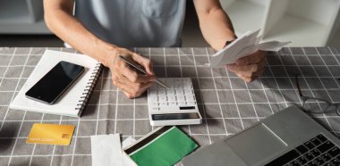 A dedicated man calculating expenses and organizing financial documents at a table, utilizing a calculator to manage his savings and budget effectively. clipart