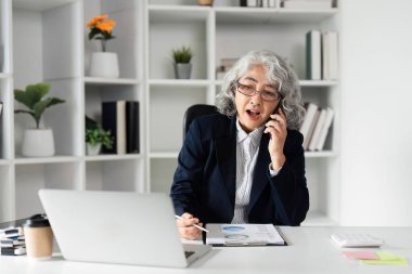 Yaşlı bir iş kadını ofisinde güvenle konuşuyor, liderlik ve yönetim becerilerini gösteriyor..