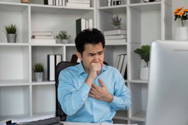 Modern ofis ortamında genç bir işadamı hasta görünüyor, masasında oturuyor, eli göğsünde, rahatsızlığını dile getiriyor..