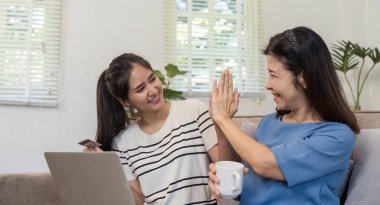 Bir anne ve çocuk mutlu bir şekilde internetten kredi kartıyla alışveriş yapar, rahat bir ev ortamında kaliteli zaman geçirirler..