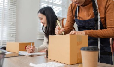 Odaklanmış kadın girişimciler gömlek siparişlerini etkili bir şekilde paketliyor, not alıyor ve şık butik ofislerinde envanter yönetiyorlar..