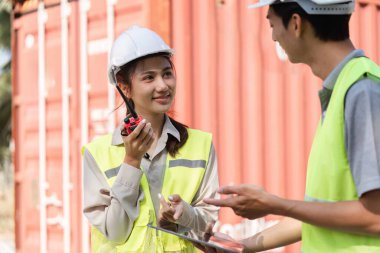 Bir lojistik mühendisi ve bir teknisyen, yoğun bir inşaat sahasında telsiz kullanarak iletişim kuruyor..