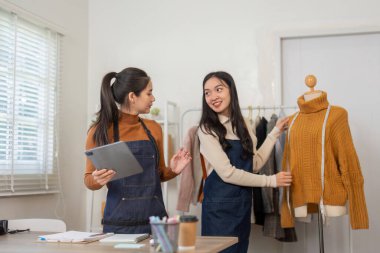 İki hevesli kadın girişimci, şık bir süveter sergilerken parlak bir butik çalışma alanında online gömlek satışlarına hazırlanırken fikir alışverişinde bulunuyorlar..
