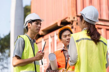 Bir yönetici, bir mühendis ve bir teknisyenden oluşan birleşik bir lojistik mühendisliği ekibi proje detaylarını tartışıyor ve bölgedeki planları inceliyor..