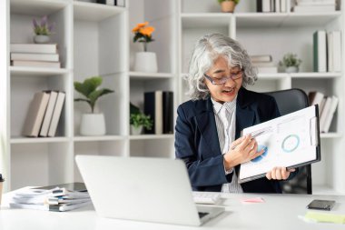 Deneyimli iş kadını online toplantı yoluyla veri sunuyor, profesyonel ofis ortamında grafik ve çizelgeleri gösteriyor.