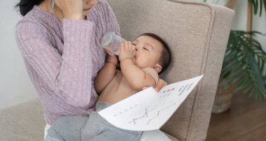 Düşünceli bir anne bebeğini beslerken düşünmek için ara verir. İş ve bakım dengesini sağlayan rahat bir ofis ortamında iş çizelgeleri tutar..