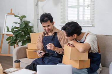 Çevrimiçi işleriyle meşgul olan iki adam, strateji tartışıyor ve iyi organize edilmiş çalışma alanlarında kutu paketliyorlar..