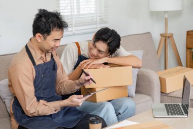 Sevgi dolu bir LGBT çifti çevrimiçi işlerine dalmış, gülümsüyor ve konforlu bir yaşam alanında kutuları tutarken stratejilerini tartışıyorlar..