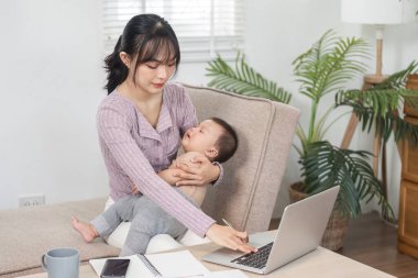 Kendini işine adamış bir anne laptopunda bebeğini sıcak bir ofiste kollarına alarak yazarken işini ve ebeveynliğini dengeler.