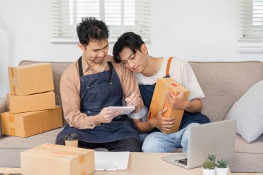 İlgili bir LGBT çifti çevrimiçi mağazalarında birlikte çalışıyor, satış stratejilerini gözden geçiriyor ve konforlu bir ev ortamında ürünleri paketliyor..