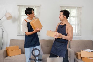İki genç Asyalı girişimci, e-ticaret işleri için lojistik konusunu tartışarak, ev ofis ortamında ürünlerini düzgünce sergiliyorlar..