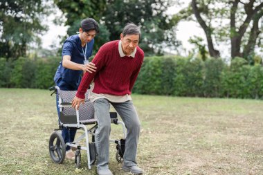 Kendini adamış bir hemşire yardımcısı, yaşlı bir adamın sakin bir bahçe ortamında tekerlekli sandalyesinden kalkmasına yardım eder. Bakıcılıktaki şefkati yansıtır..