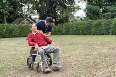 İlgili bir hemşire yardımcısı, tekerlekli sandalyedeki yaşlı bir adama yaklaşarak huzurlu bir bahçe ortamında sıcak ve destekleyici bir atmosfer yaratıyor..