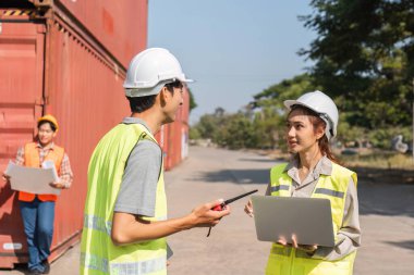 Proje detayları üzerinde çalışan üç inşaat işçisi, bir erkek denetçi ve kadın mühendis konteynerlerin önünde planları tartışıyorlar..