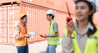 Güvenlik yelekleri ve işçileri olan bir mühendis de dahil olmak üzere dinamik bir inşaat ekibi, iş birliği ve fikir alışverişinde bulunurken, bir meslektaşı da iş yerinde telsizle iletişim kuruyor..