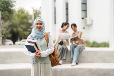 Arkadaşları bir üniversite kampüsünün arka planında çalışmalar yaparken ve gururunu ve akademik ruhunu sergilerken kendine güvenen farklı bir kız öğrenci elinde kitap tutuyor..