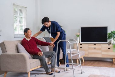 Hemşire, yürütecinden, güneşli bir oturma odasındaki rahat ve iyileşme sürecinde yaşlı bir adama yardımcı olur..