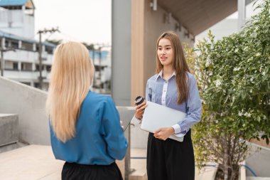 İki farklı iş kadını fikir alışverişinde bulunurken, biri dışarıda bir çalışma alanında dizüstü bilgisayar ve kahve bardağı tutuyor ve yaratıcı bir değiş tokuşun reklamını yapıyor..
