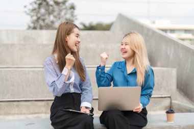 İki farklı iş kadını başarılı bir fikri sevinçle kutlarken açık havada dizüstü bilgisayar ve tablet kullanıyorlar, takım çalışması ve coşku sergiliyorlar..