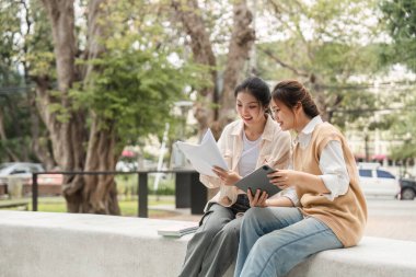 İki farklı öğrenci çalışma materyallerini değerlendiriyor ve üniversite ortamında dışarıda otururken tartışıyorlar..