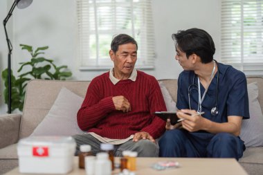 Bir hemşire, parlak bir oturma odasında oturan yaşlı bir adamla birlikte önemli sağlık bilgilerini gözden geçirir ve ziyaret sırasında anlayış ve bakım sağlar..