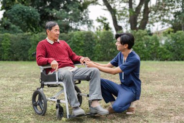 Bir hemşire yardımcısı, tekerlekli sandalyedeki yaşlı bir adamla iletişim kurar. Huzurlu bir bahçe ortamında huzur ve bakım sağlar. Bakıcı ve hasta arasındaki bağı gösterir..