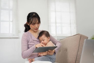 Bir anne ve bebeği rahat bir ev ortamında etkileşimli tablet vakit geçiriyorlar, öğrenme ve iletişimi teşvik ediyorlar..