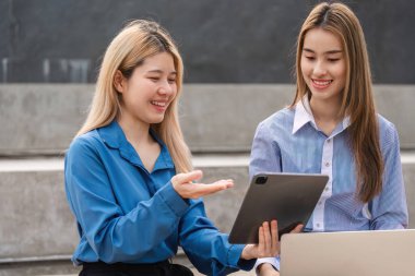 İki farklı kadın bir tablet üzerinde birlikte çalışıyor, fikirleri paylaşıyor ve çağdaş bir açık havada işbirliği yapıyorlar..