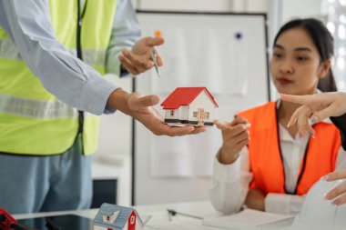 Çeşitli bir inşaat ekibi, ortak bir toplantı sırasında minyatür bir ev modelini analiz ederek proje planlamasına olan bağlılıklarını gösterdiler..