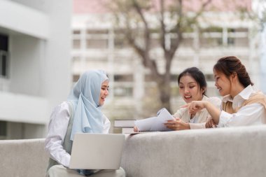 Açık havada birlikte okuyan üç farklı kız öğrenci, üniversite ortamında notlarını ve dizüstü bilgisayarlarını paylaşırken tartışmaya giriştiler..