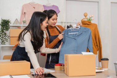 İki farklı kadın e-ticaret çalışanı perakende mağazasında kıyafet düzenlerken giyimlerini tartışıyor ve sergiliyorlar..